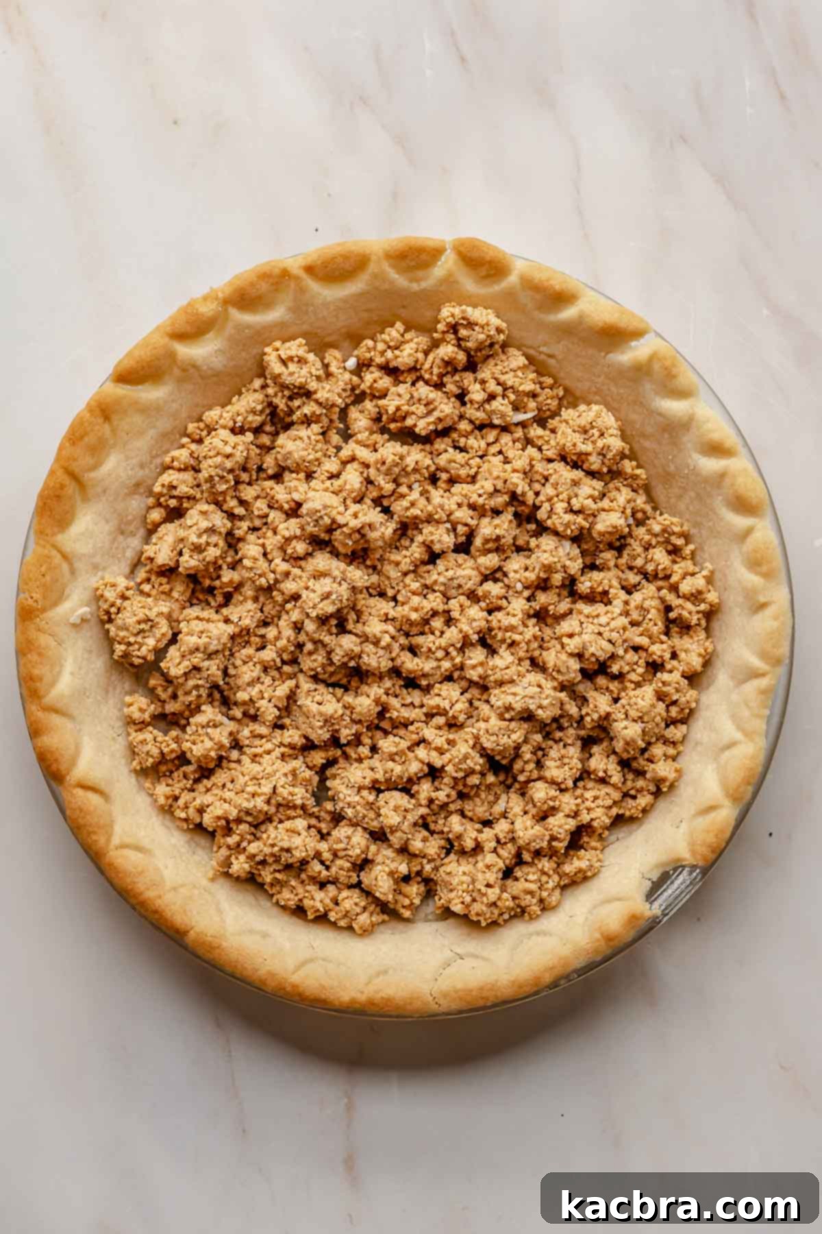 Peanut butter crumbles evenly spread in the bottom of a baked pie crust.