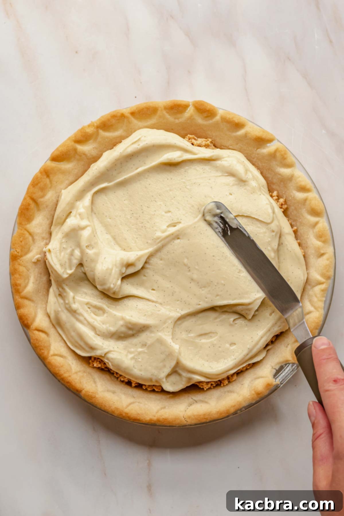 An offset spatula smoothly spreading vanilla pudding over the peanut butter crumbles in the pie crust.