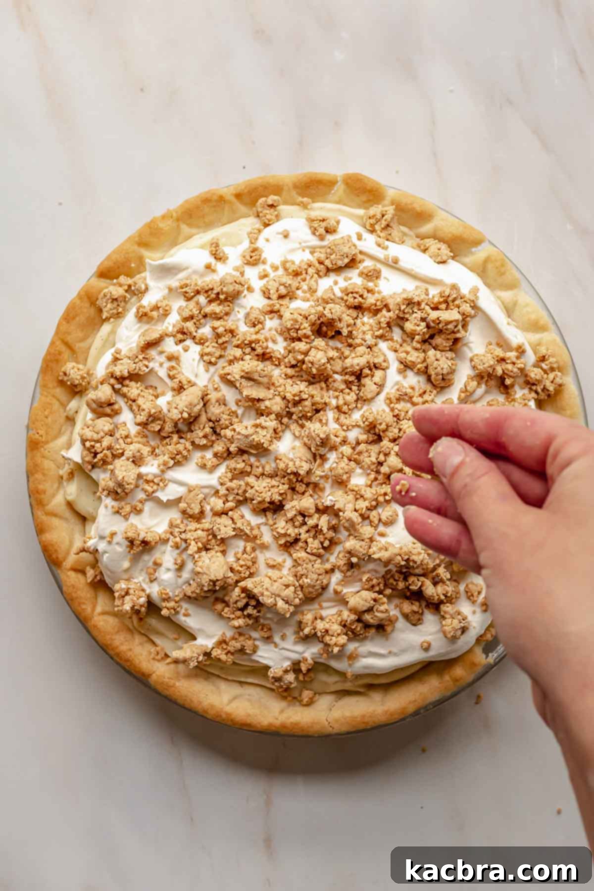 A hand sprinkling the remaining peanut butter crumbles over the whipped cream topping of the pie.