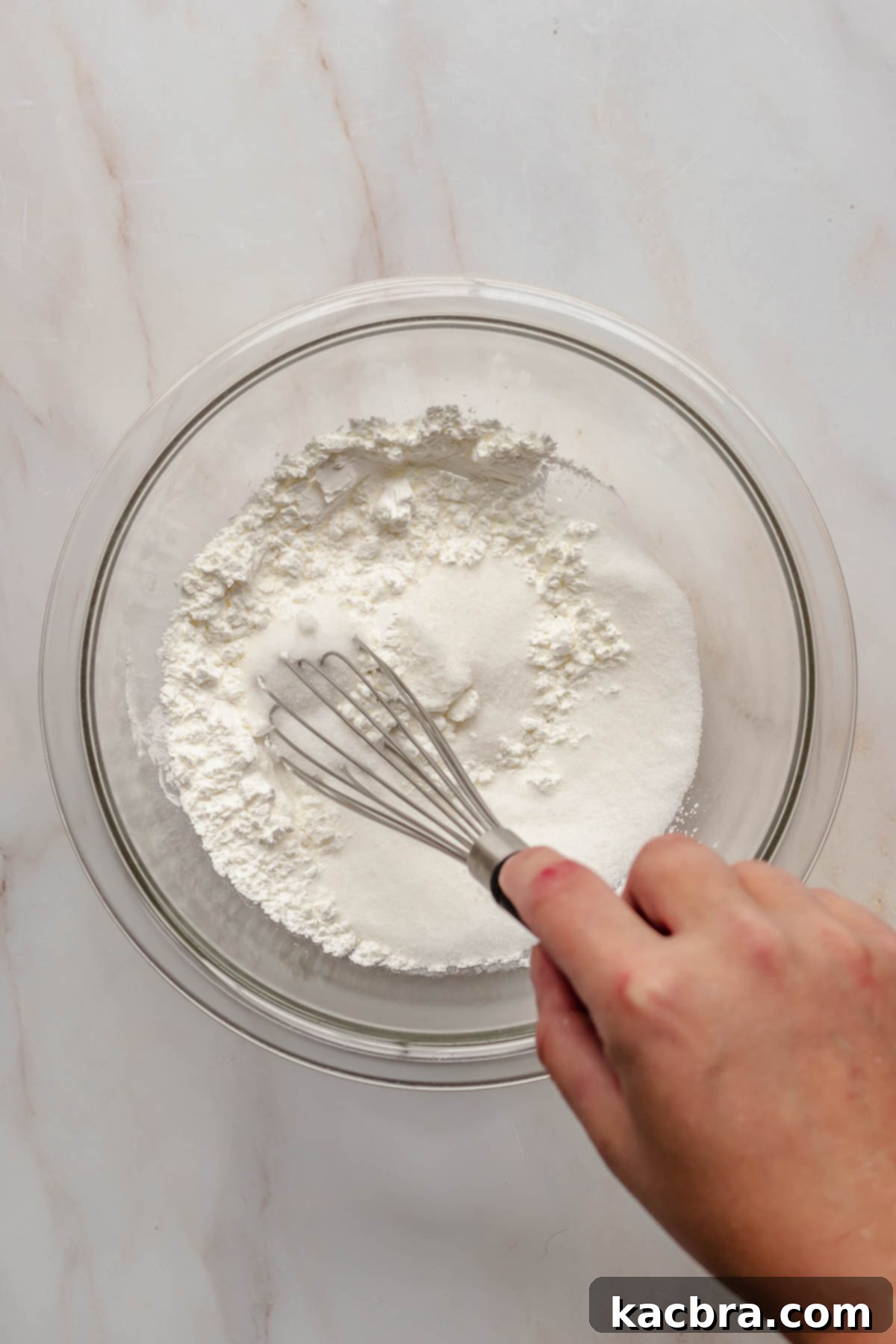 A hand whisking granulated sugar and cornstarch together in a bowl.