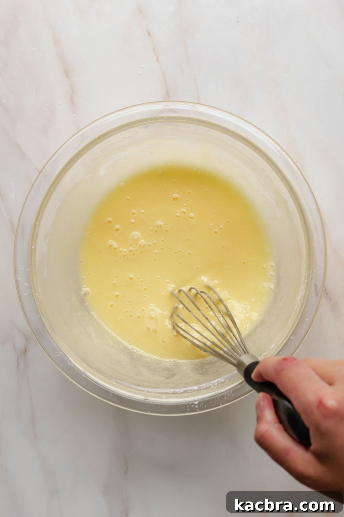 A hand whisking egg yolks into the sugar and cornstarch mixture in a bowl.