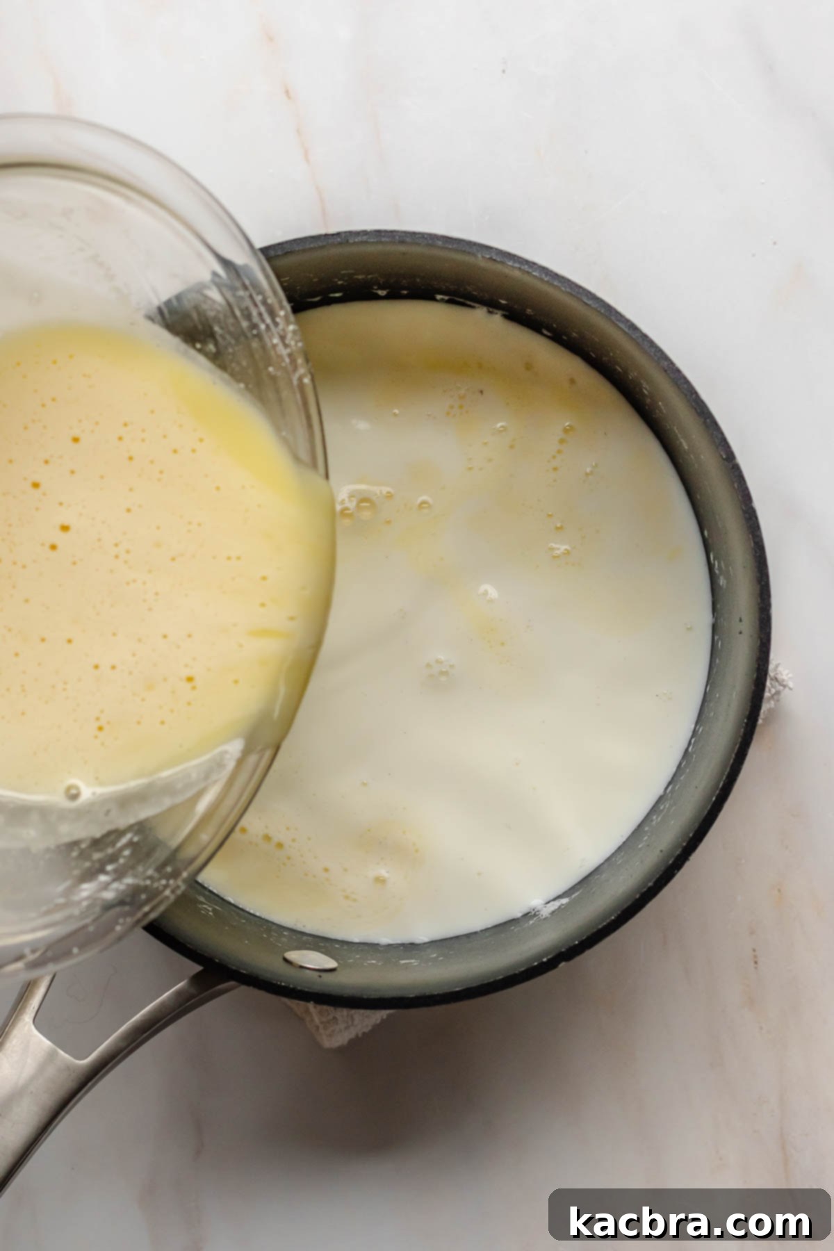 The tempered egg and milk mixture being poured back into the saucepan with the remaining hot milk.
