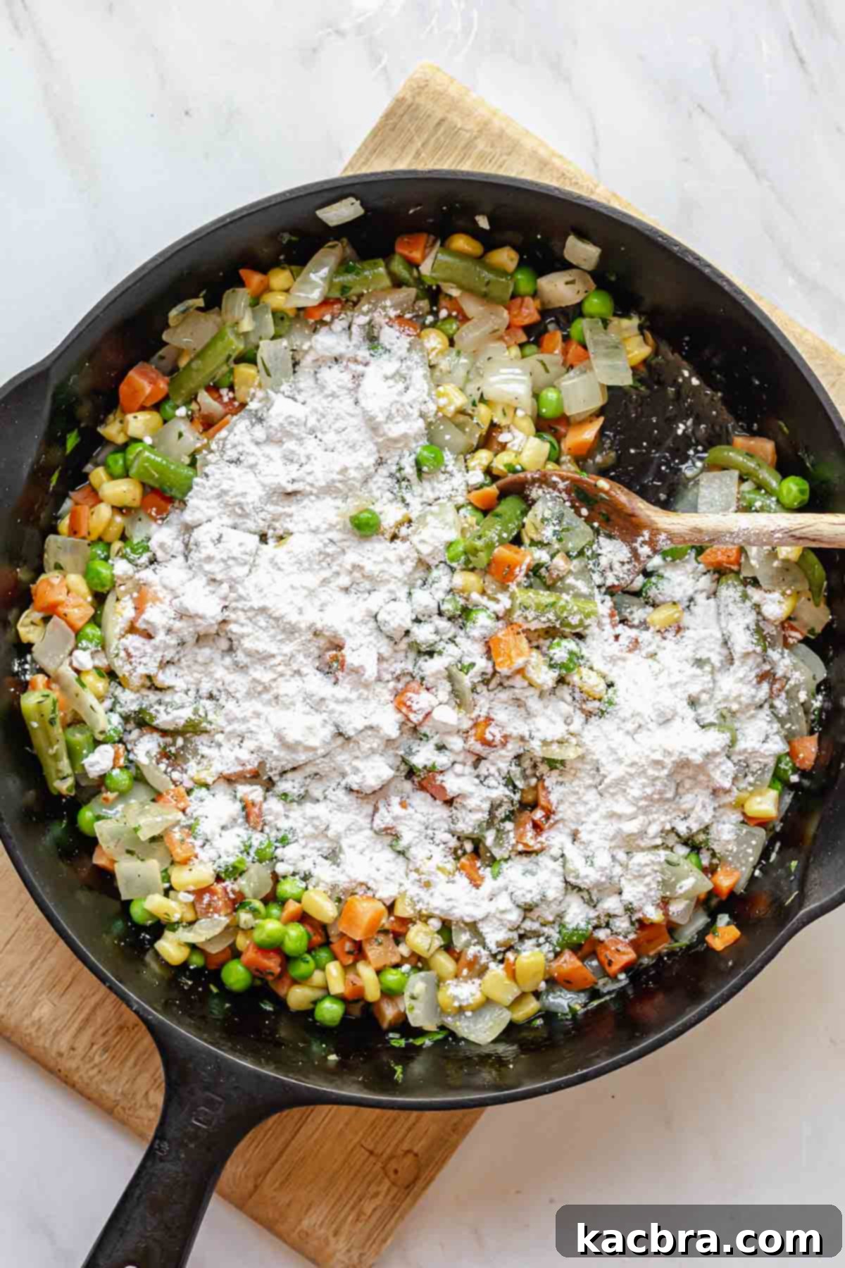 A generous sprinkling of all-purpose flour over mixed vegetables and herbs in a pan, ready for stirring.