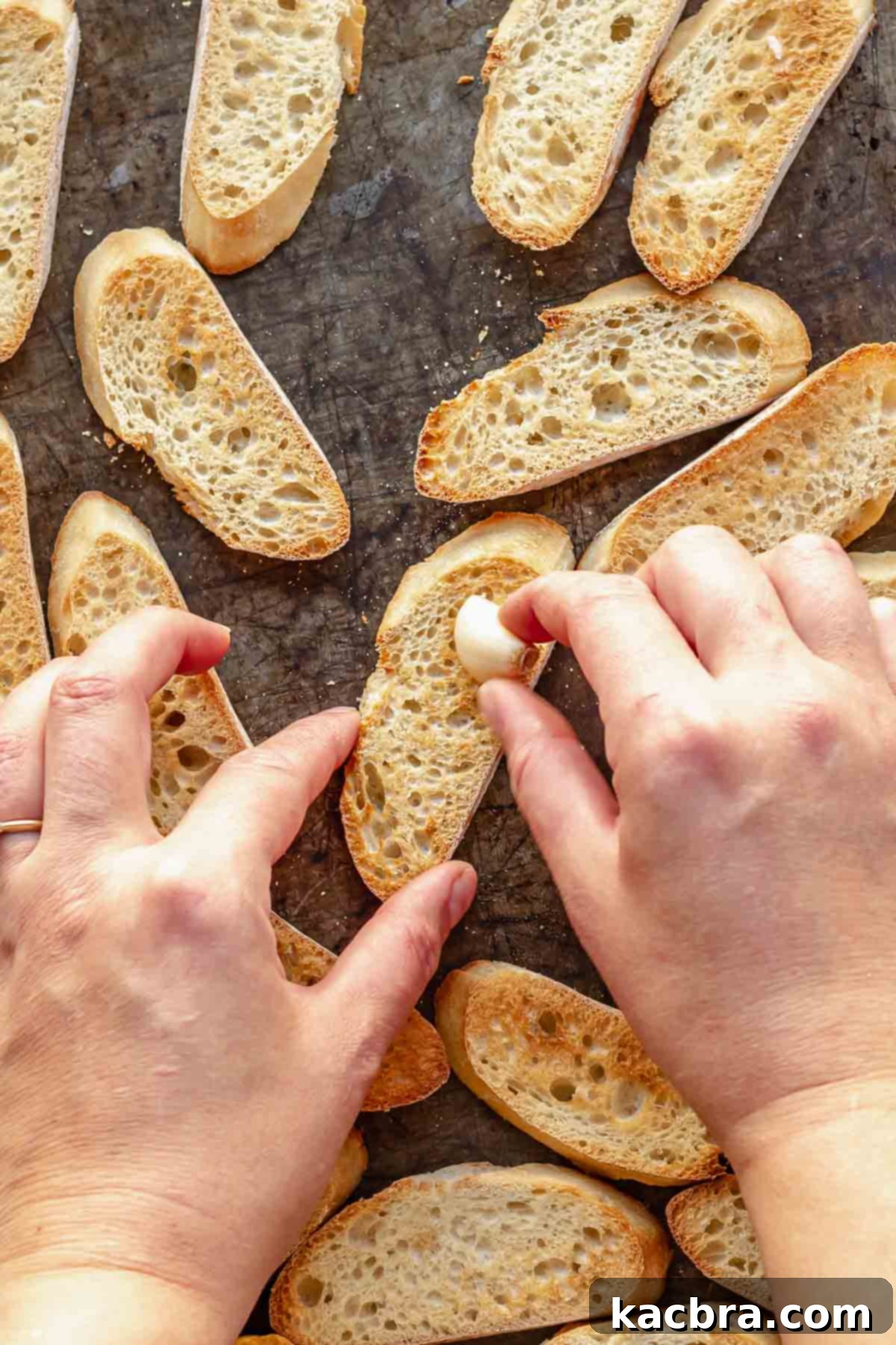 Fluffy Ricotta Crostini 6 A hand rubs a piece of garlic on toasted baguette slices.