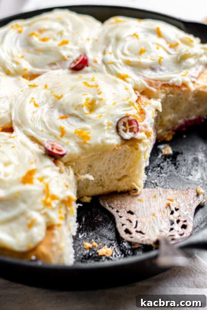 Soft and fluffy Cranberry Orange Rolls topped with orange cream cheese frosting, ready to be served on a white plate.