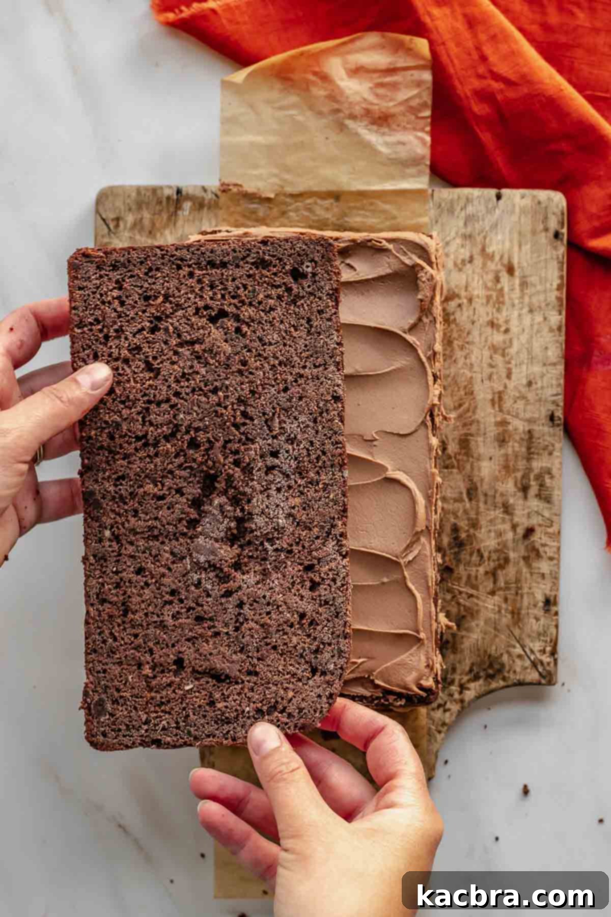 Decadent Chocolate Orange Bliss 13 Two hands add a layer of chocolate cake onto frosting, carefully stacking the cake layers.