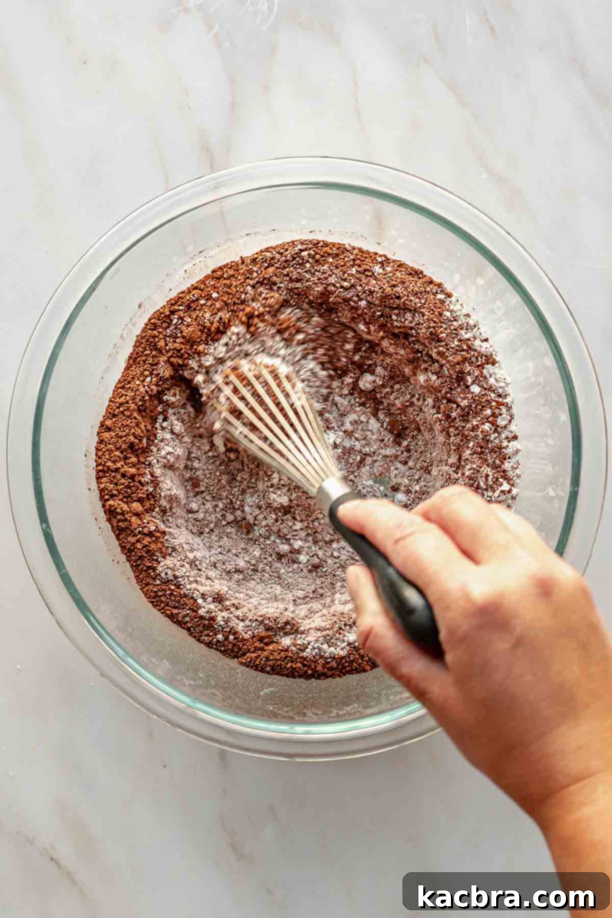 Decadent Chocolate Orange Bliss 5 A hand gently whisks together the dry ingredients for the chocolate cake in a spacious mixing bowl, ensuring an even distribution of flour, cocoa, sugar, and leavening agents.