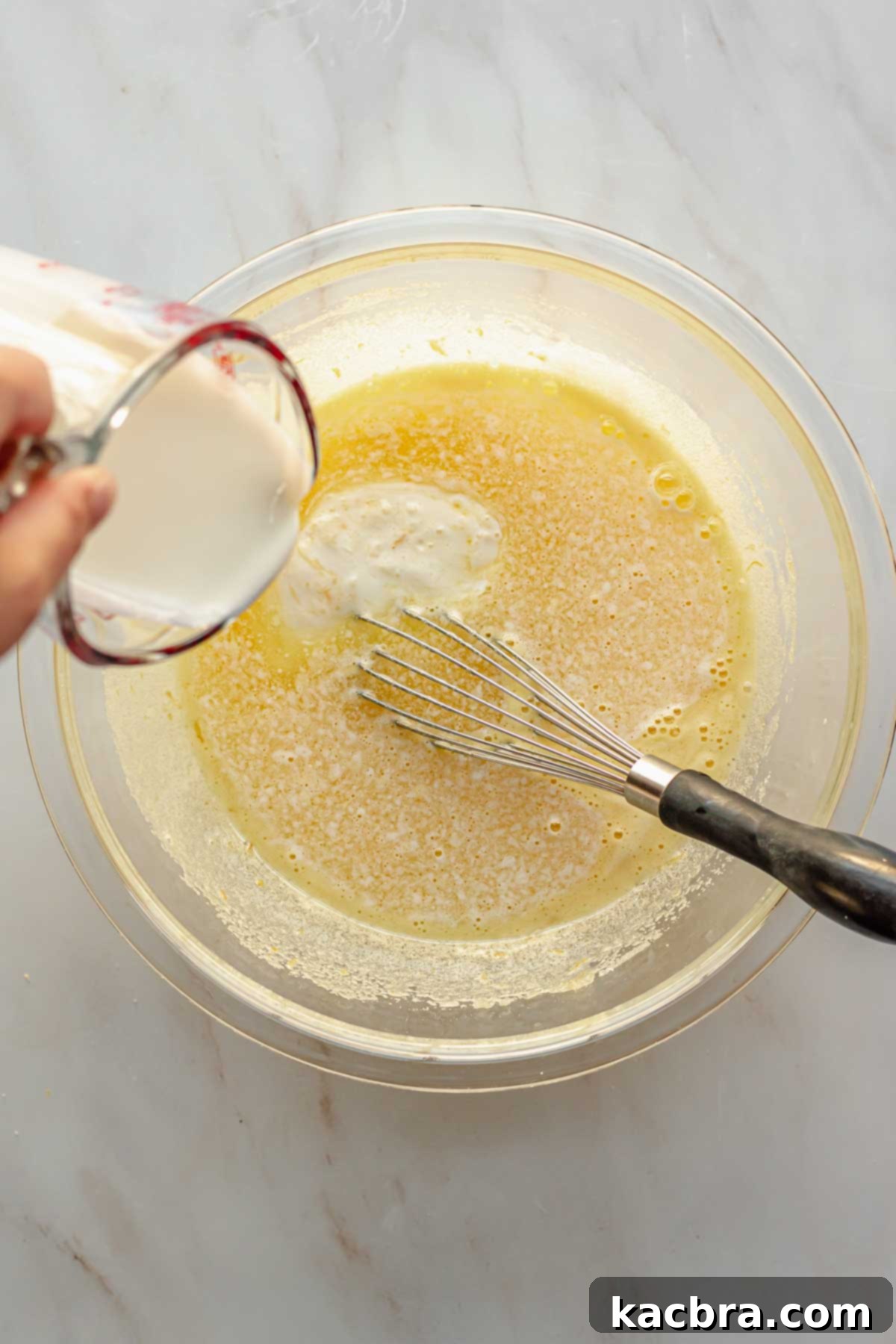 Decadent Chocolate Orange Bliss 6 A stream of creamy buttermilk being poured into a bowl of whisked wet ingredients for the cake, creating a smooth and well-incorporated mixture.