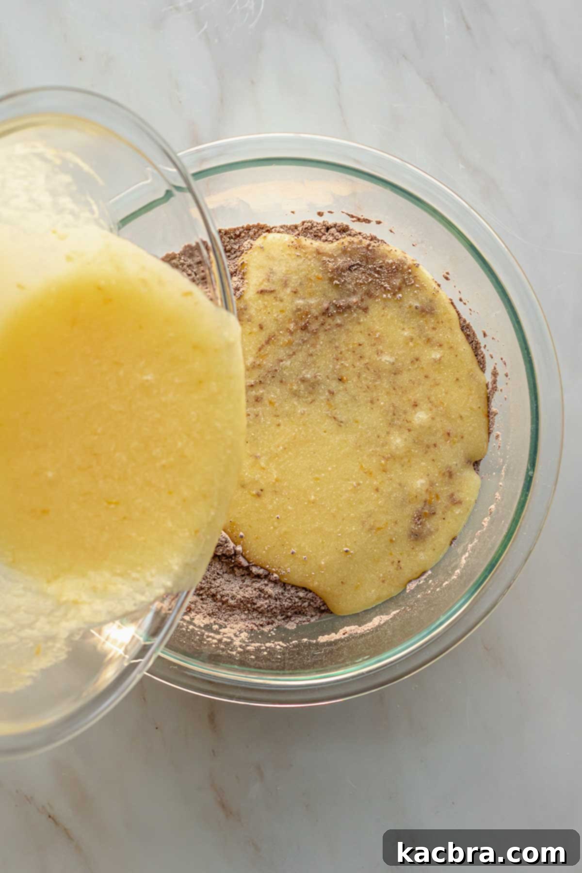 Decadent Chocolate Orange Bliss 7 The smoothly blended wet ingredients for the chocolate cake being carefully poured into the bowl containing the dry ingredients, ready for gentle mixing.