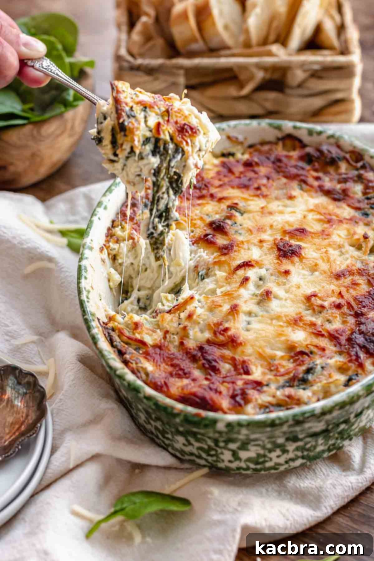 A spoon pulls out a cheesy bite of hot crab spinach dip, showcasing melted cheese and chunks of crab and spinach.