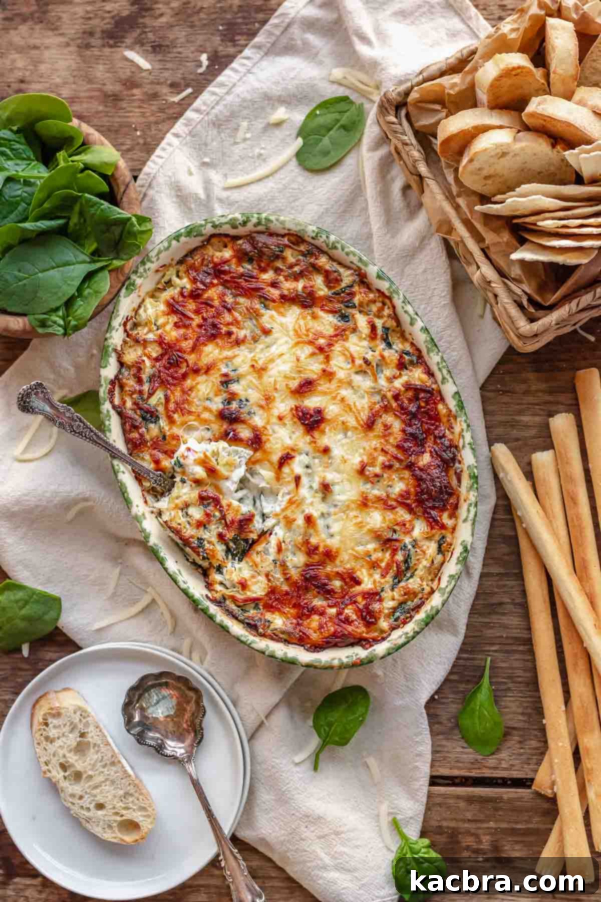 A spoon is inserted into a piping hot, bubbly, and golden-brown baked crab spinach artichoke dip.