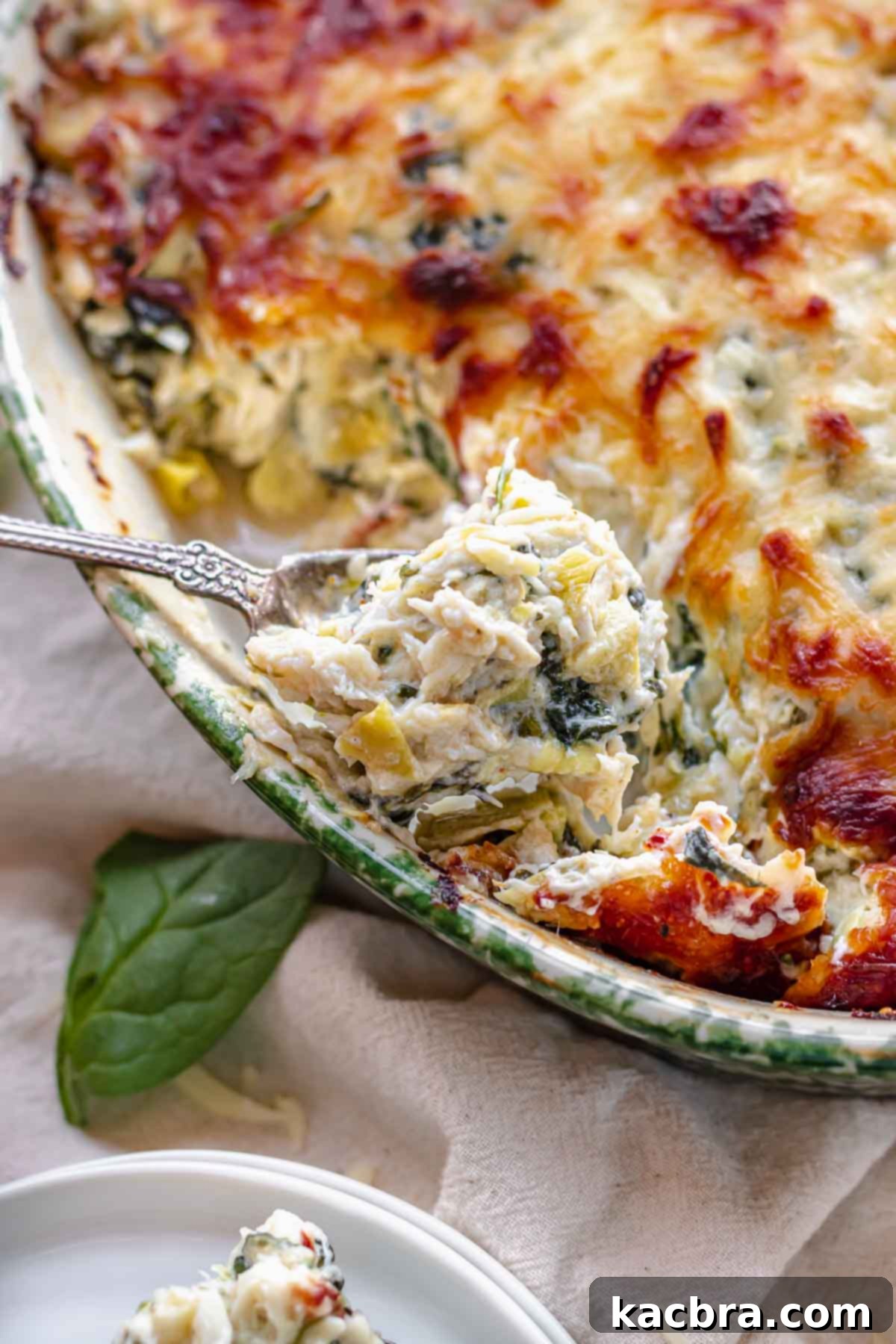 A close-up of a spoonful of hot crab spinach artichoke dip, showing its creamy, cheesy texture with visible crab and spinach.