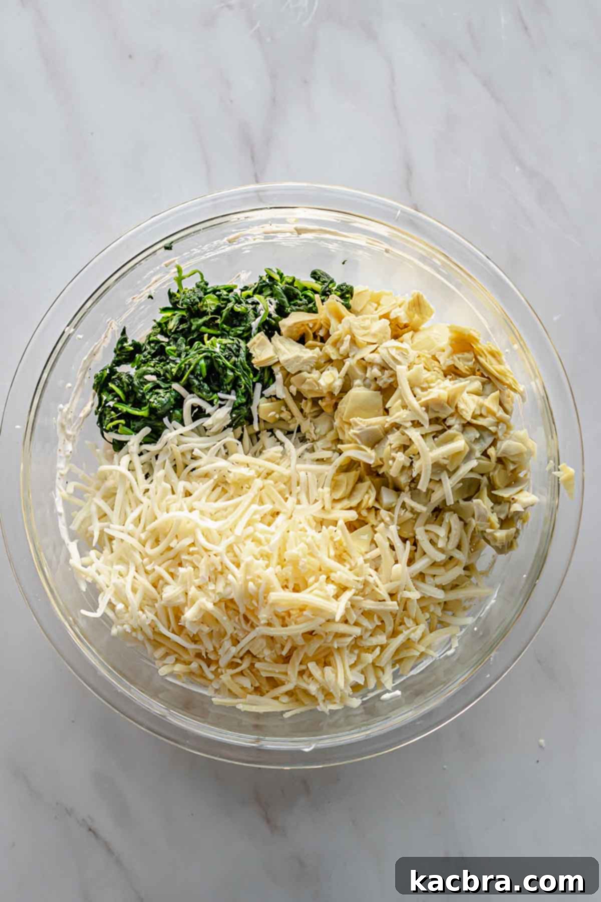 Shredded cheeses, chopped artichokes, and chopped spinach are added into a large mixing bowl.
