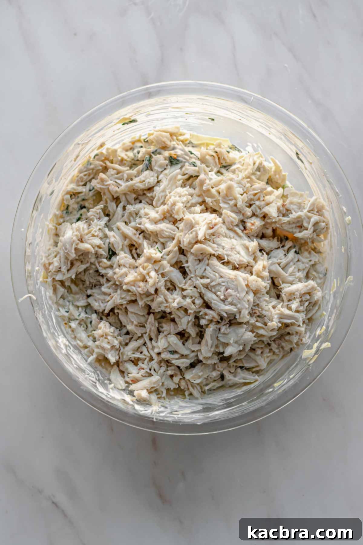 Lump crab meat is placed on top of the mixed spinach artichoke dip in a bowl.