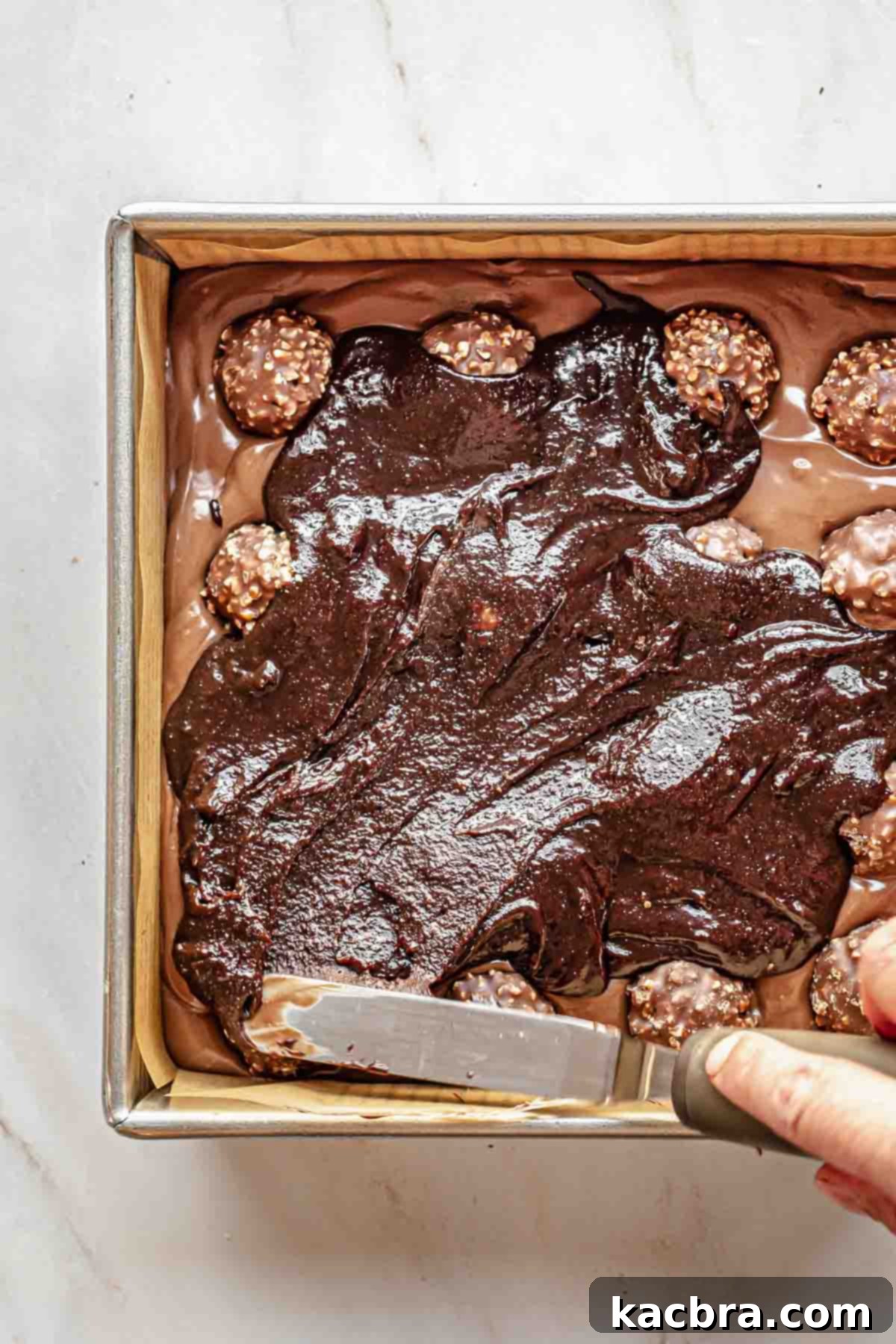 A spatula spreads brownie batter over the Ferrero rocher.