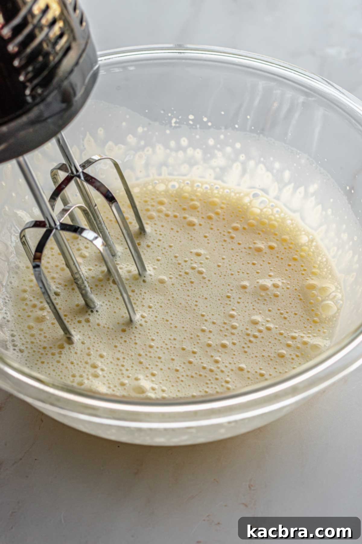 A hand mixer mixing wet ingredients in a bowl.