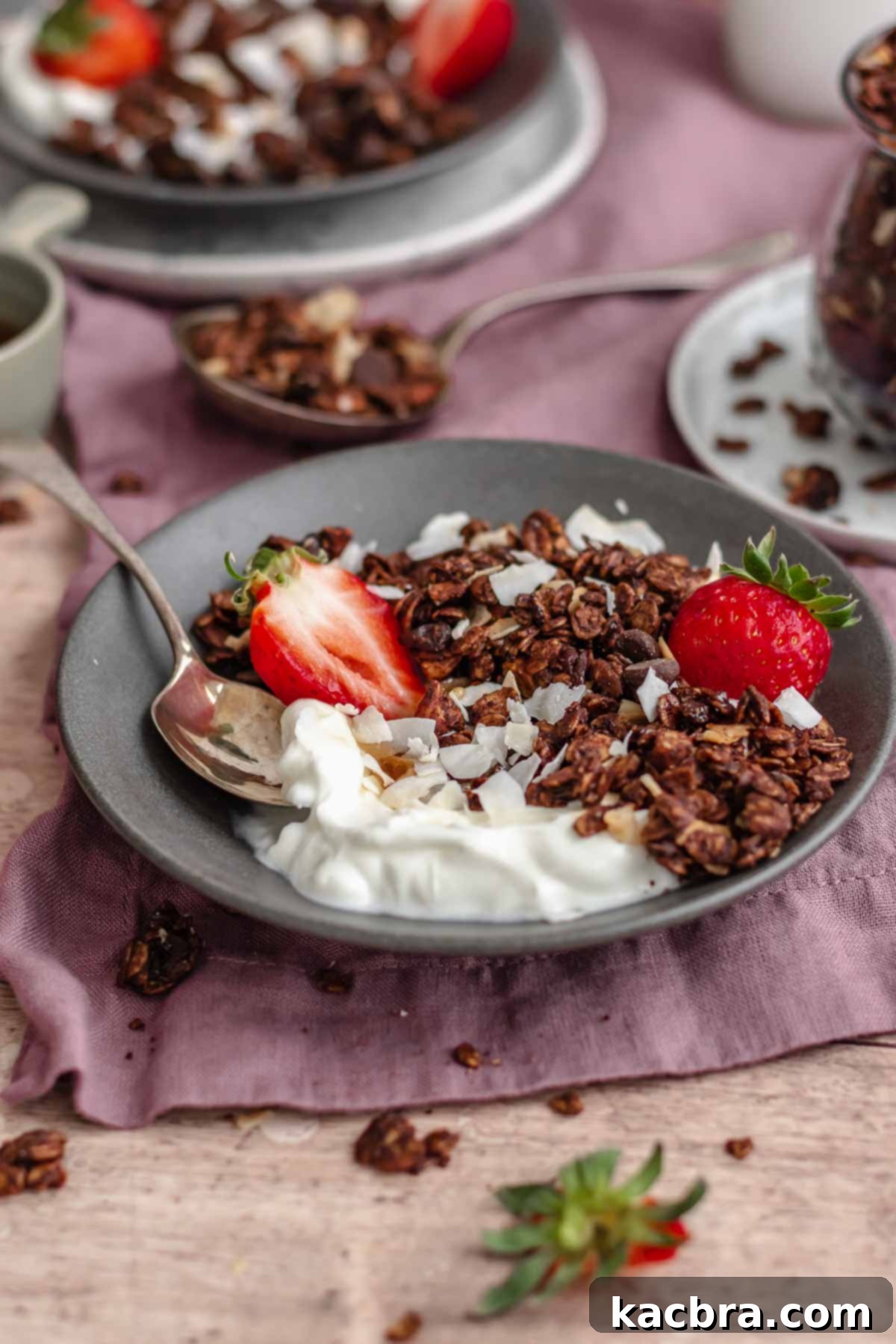 Granola and yogurt in a bowl with a spoon and strawberries.