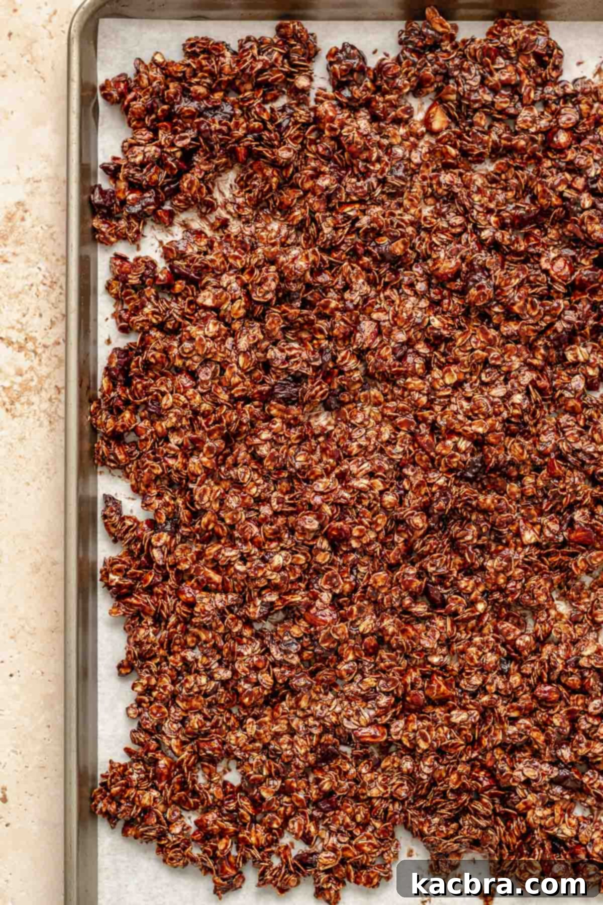 Granola mixture spread evenly on a parchment-lined sheet pan, pre-baked.