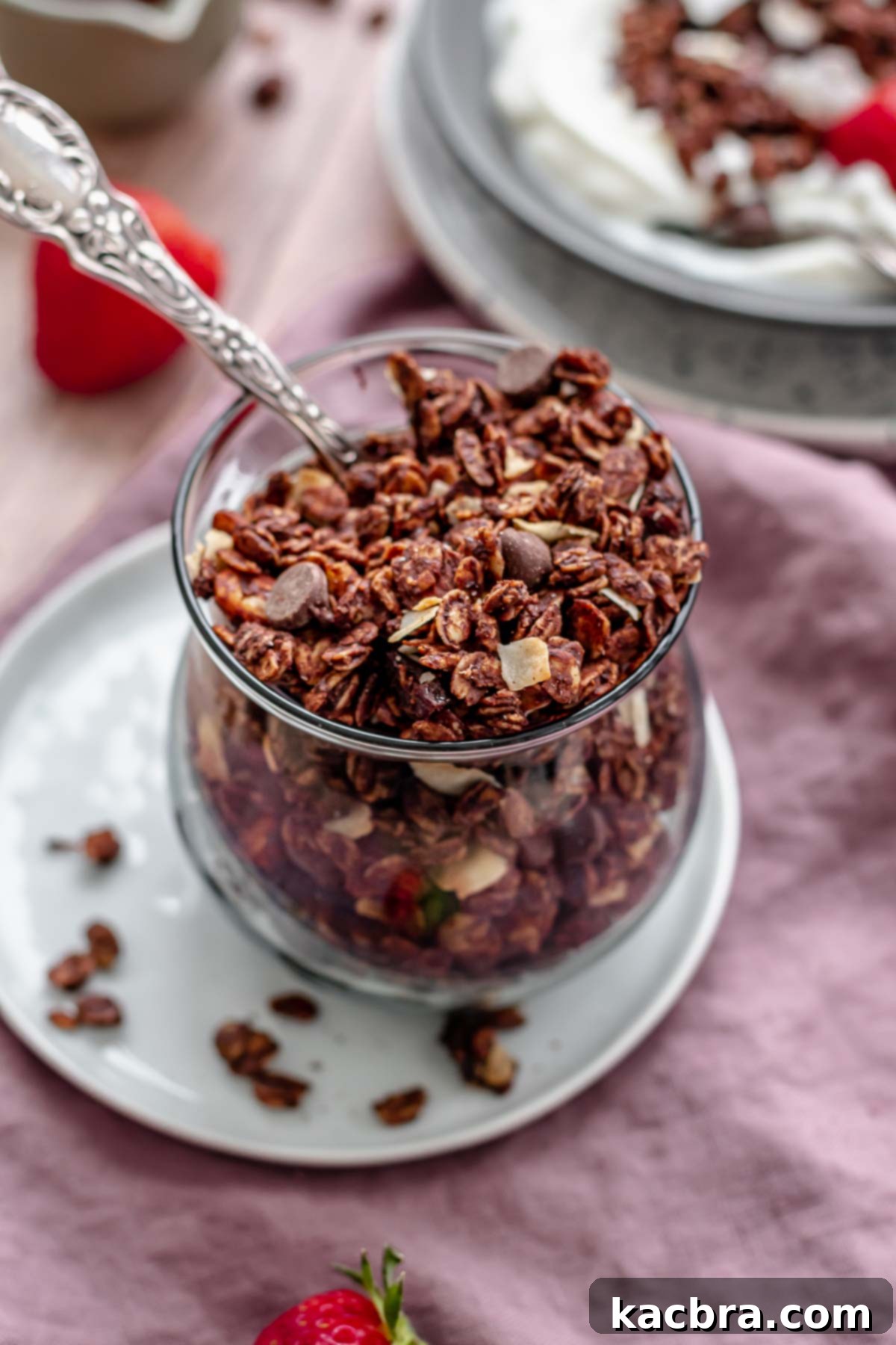 Finished chocolate granola in a cup with a spoon in it, ready to enjoy.