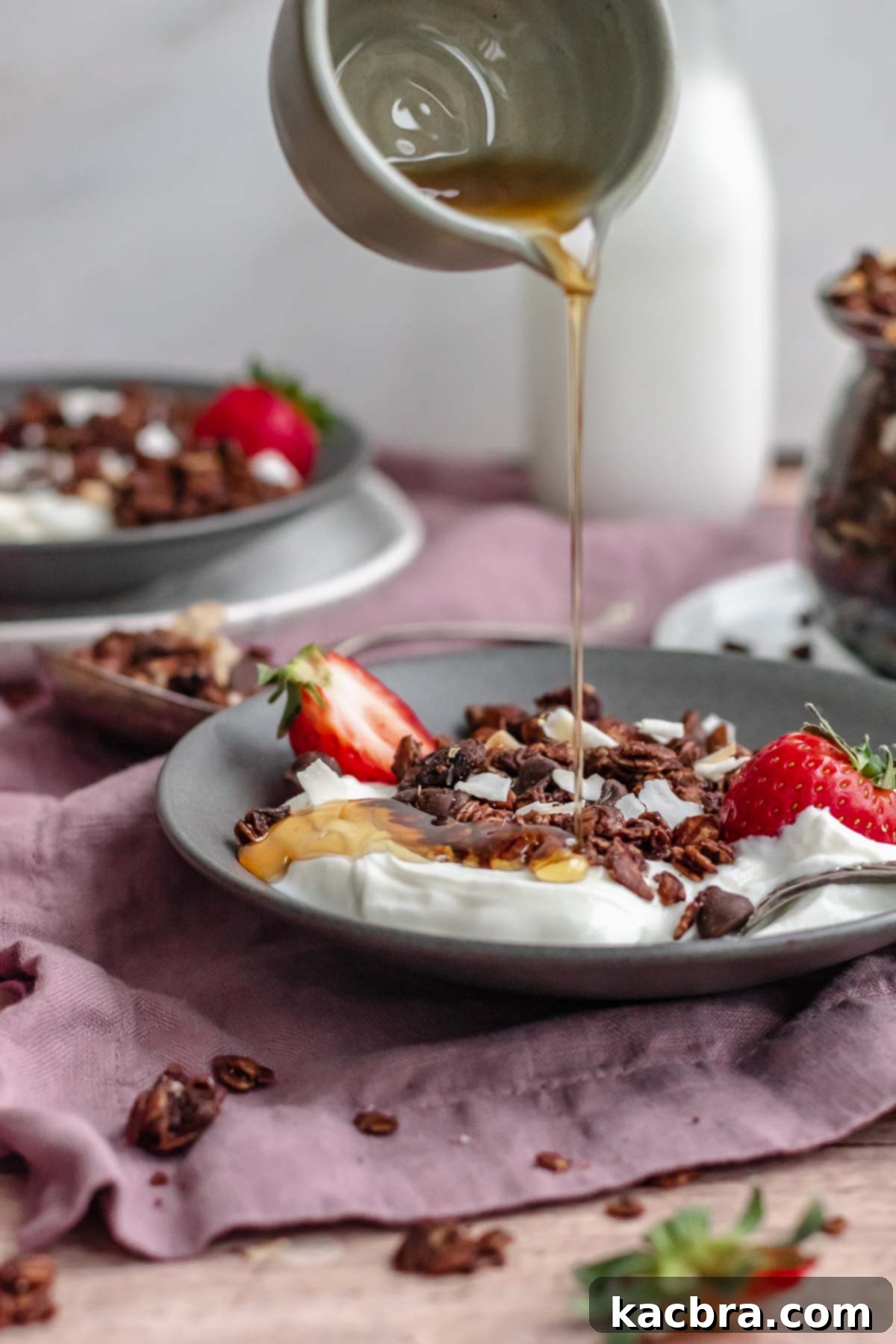 Maple syrup being poured over a bowl of yogurt and chocolate granola.
