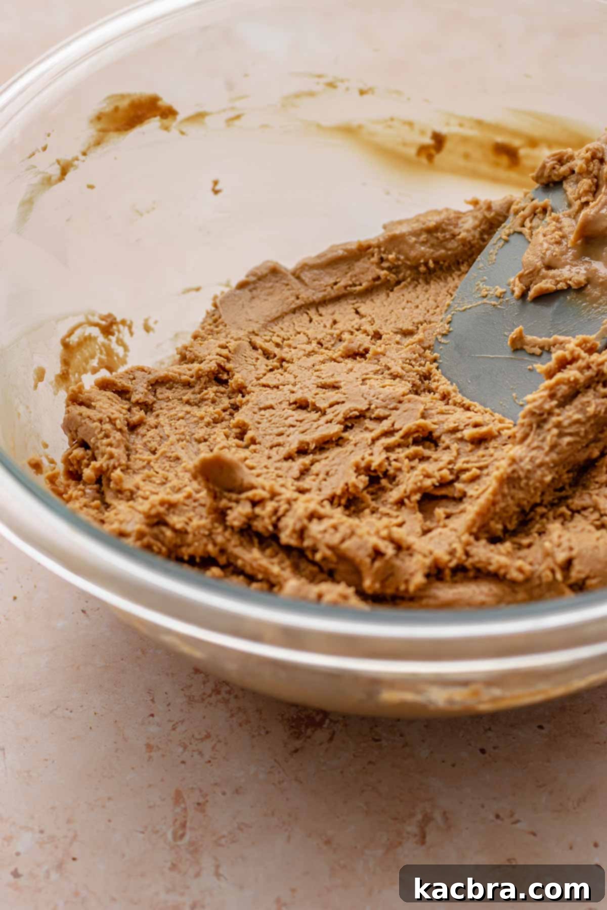 A spatula mixing Biscoff cookie butter fudge in a large bowl, showing its thickening consistency.
