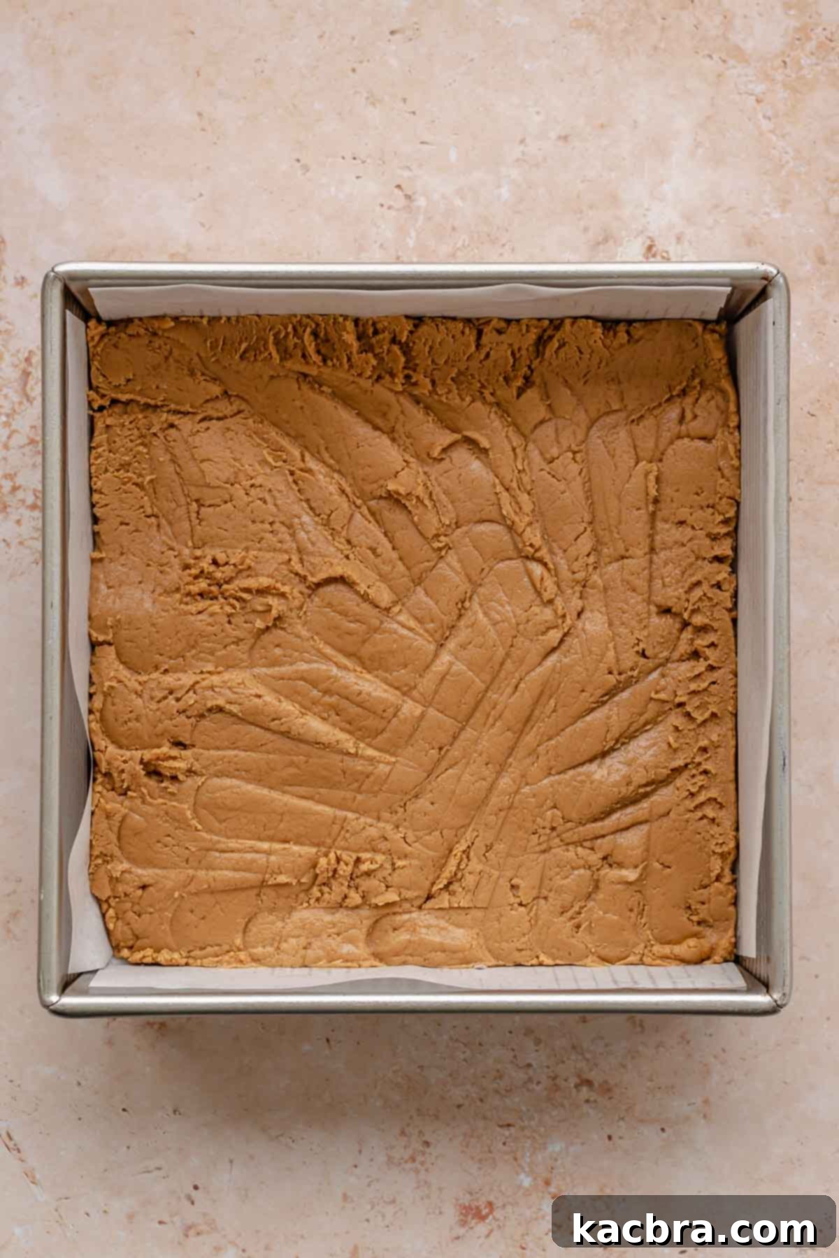 Half of the Biscoff cookie butter fudge pressed evenly into a parchment-lined 8x8 inch pan.