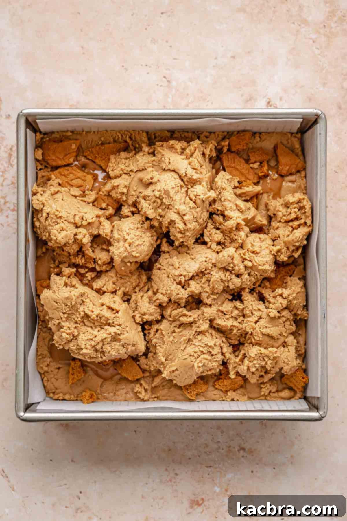 Biscoff fudge in a pan with dollops of the remaining fudge mixture before being smoothed out.
