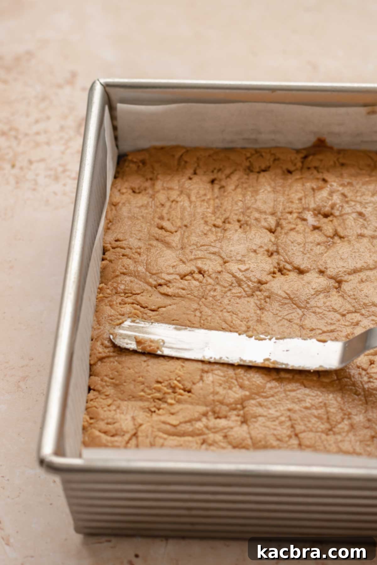 A spatula smoothing the Biscoff fudge flat and evenly into the pan.