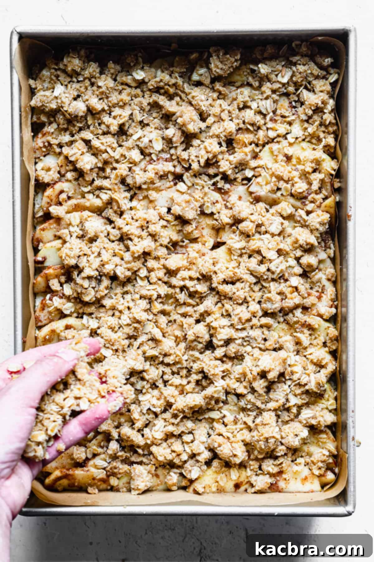 A hand sprinkles streusel topping on top of the apples.