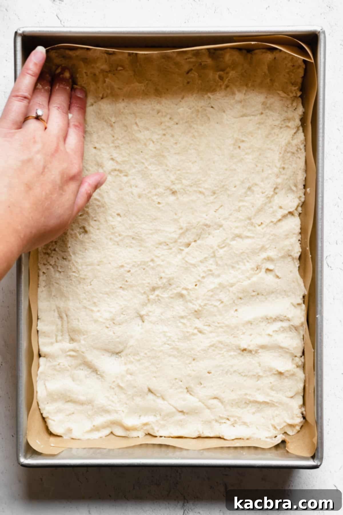 A hand presses the shortbread evenly into the pan.