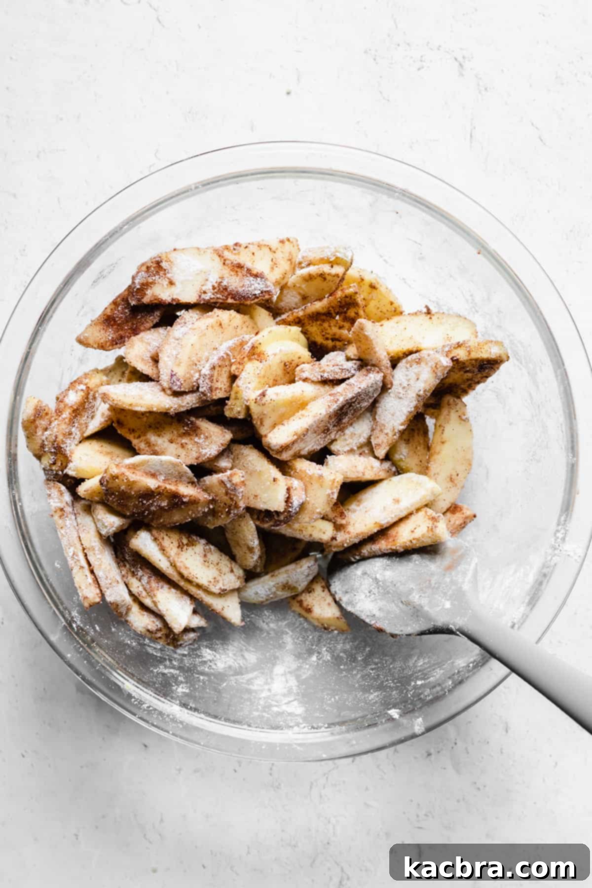 A rubber spatula mixes together spiced apple slices.