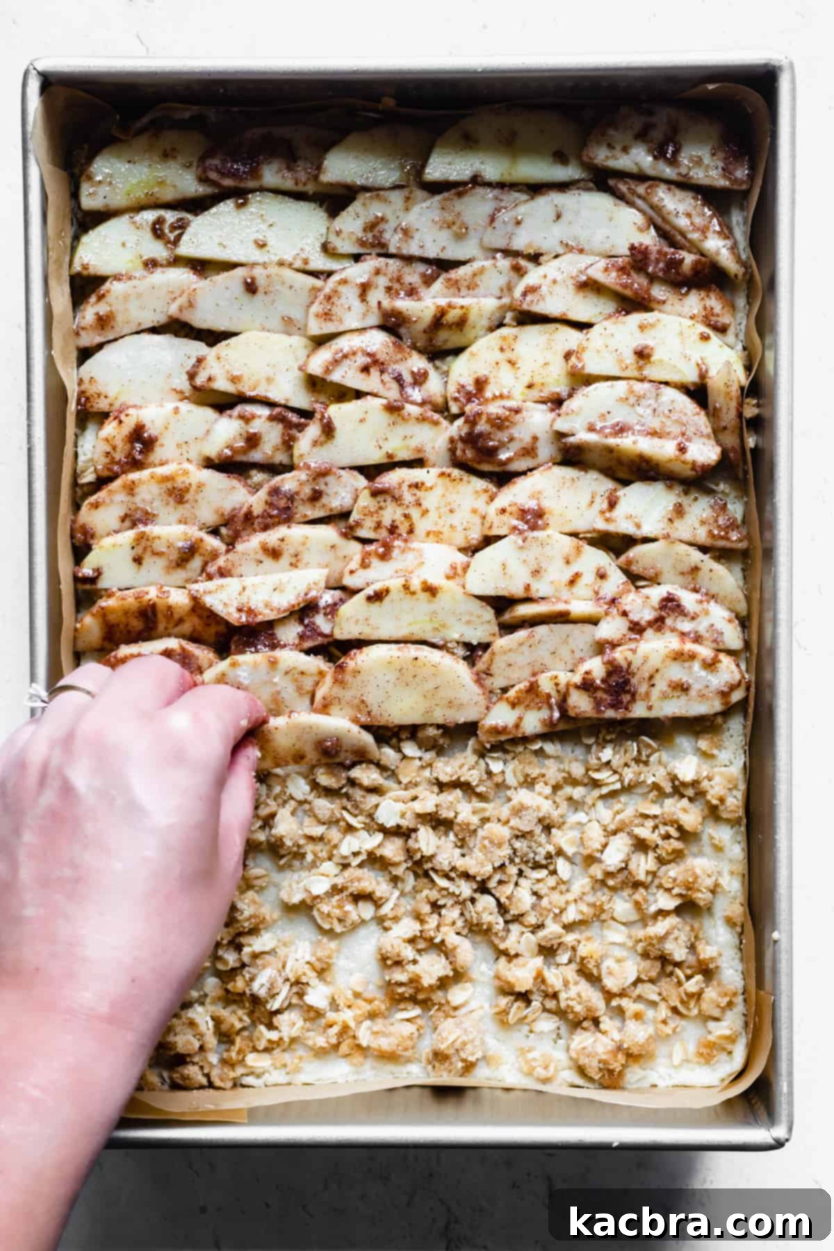 A hand adds apples in a layer on the shortbread base.