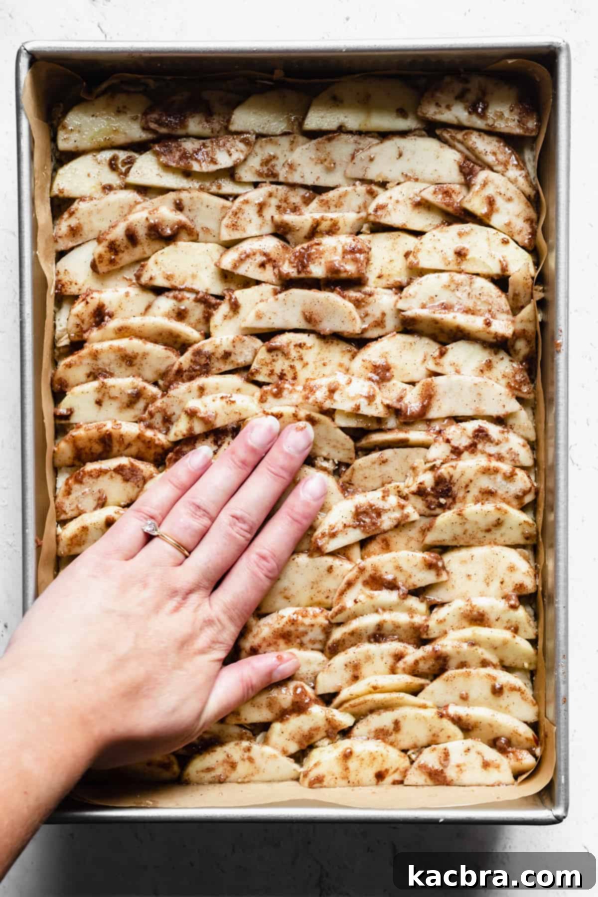 A hand presses down on apple slices layered on top of shortbread.