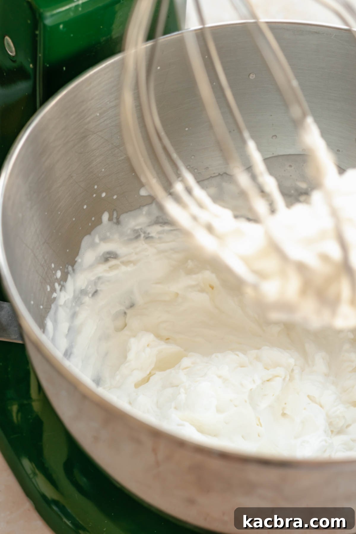 Whipped cream in a bowl with some on the tip of the whisk, showing stiff peaks.
