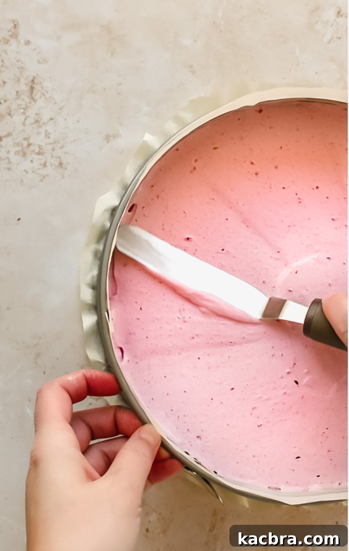 A spatula smoothing raspberry mousse evenly over the chocolate cake base.