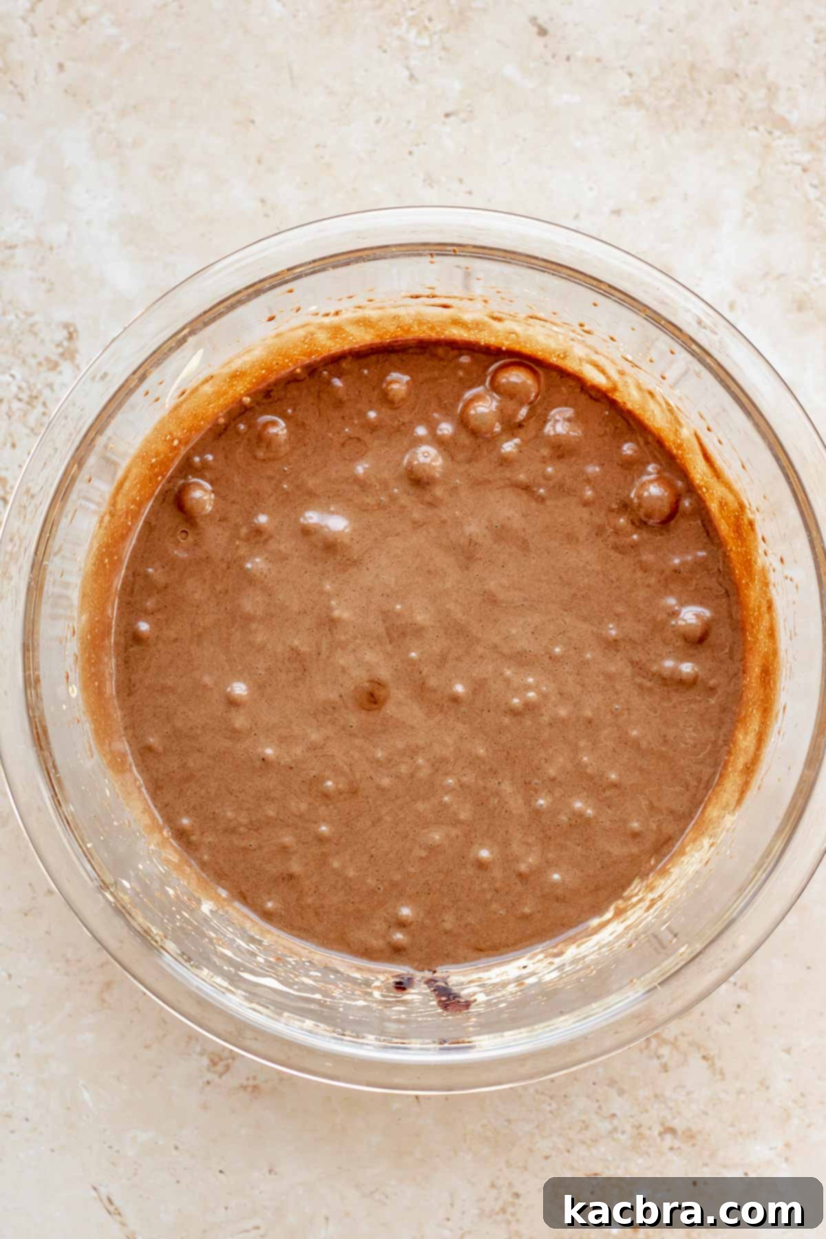 Chocolate batter being added to whisked eggs and sugar in a bowl.