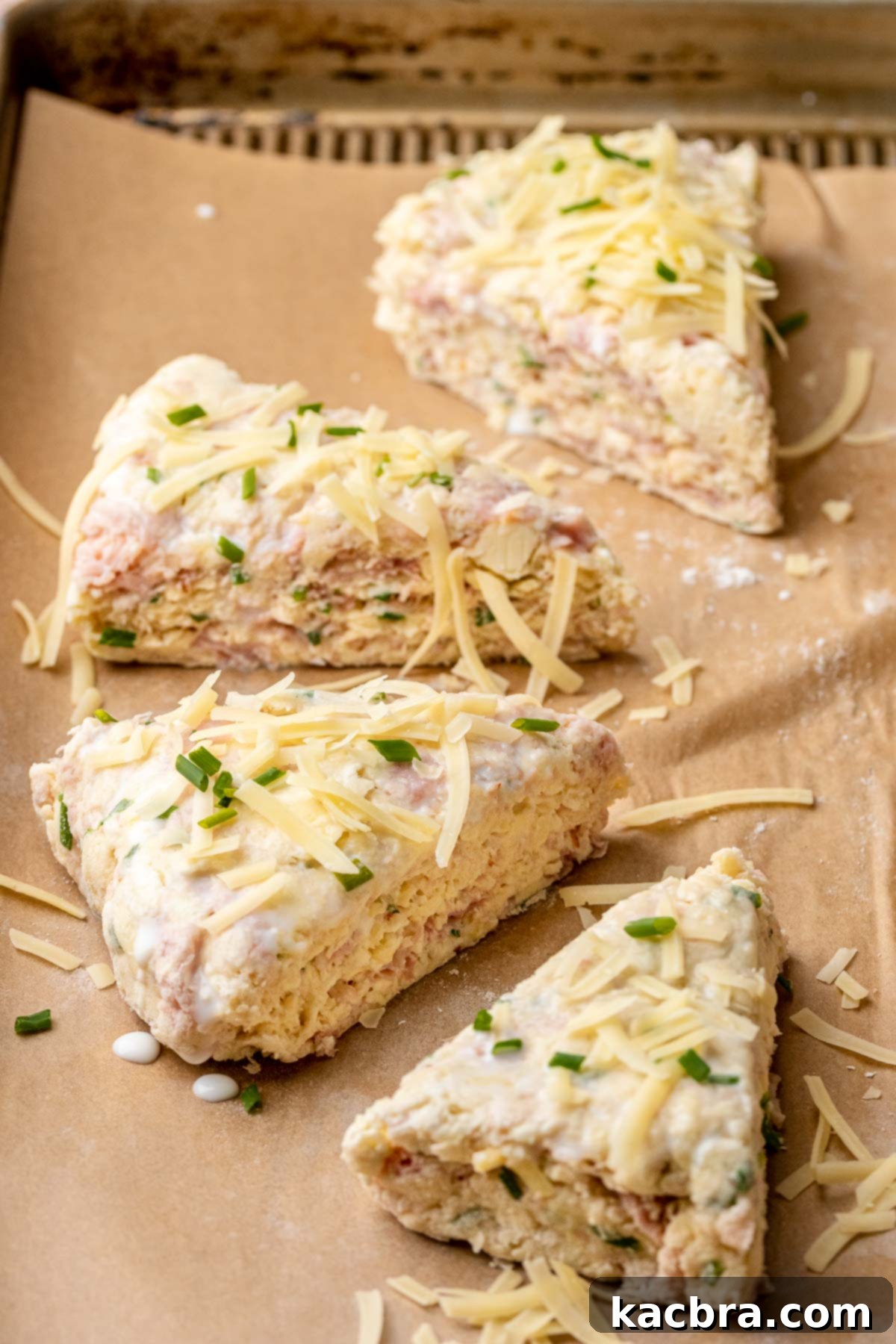 Ham and cheese scones, generously topped with extra cheese and fresh chives, ready to be baked to golden perfection. The image showcases the final touches before baking, highlighting the flavorful toppings.