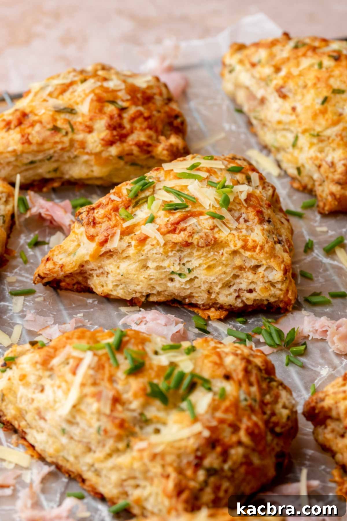 A batch of freshly baked ham and cheese scones, resting on parchment paper after being removed from the oven. The image captures their golden-brown color, slightly irregular shapes, and the aroma of warm, savory goodness.