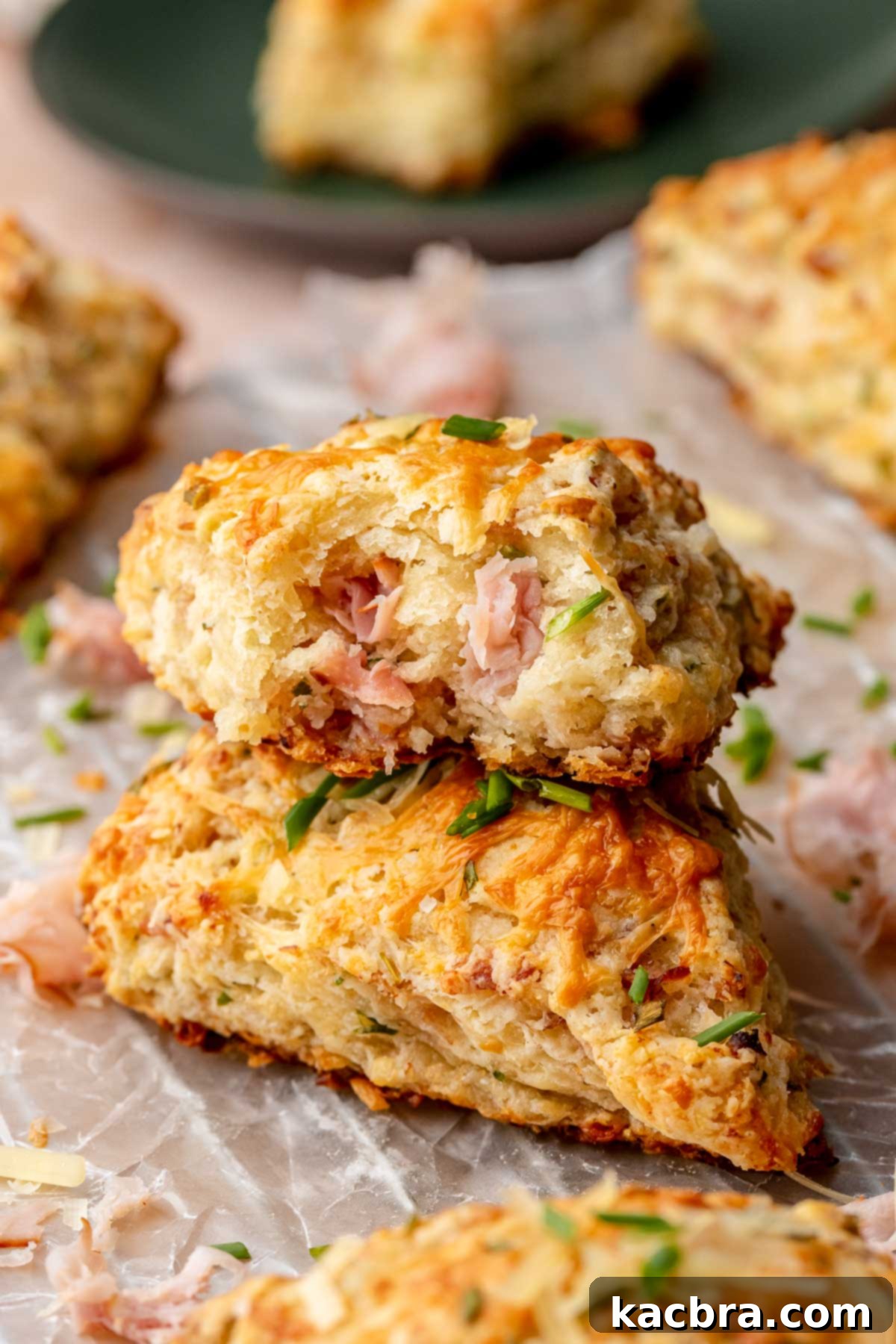 A mouthwatering stack of freshly baked ham and cheese scones. The top scone has a bite removed, revealing the soft, cheesy interior and inviting you to indulge.
