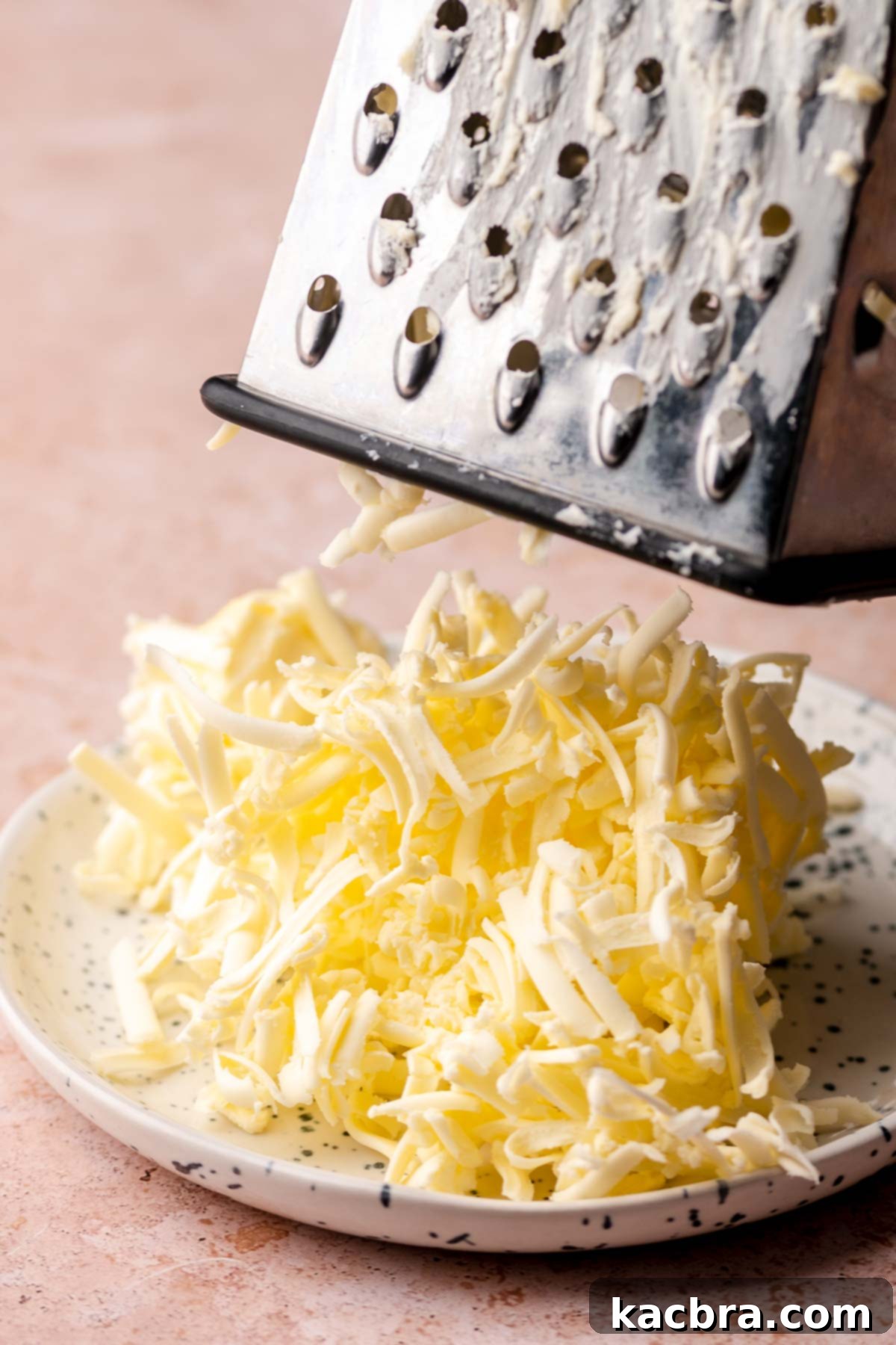 A close-up shot showcasing the process of grating frozen butter using a box grater. The image emphasizes the importance of using cold butter to achieve the desired flaky texture in the scones.