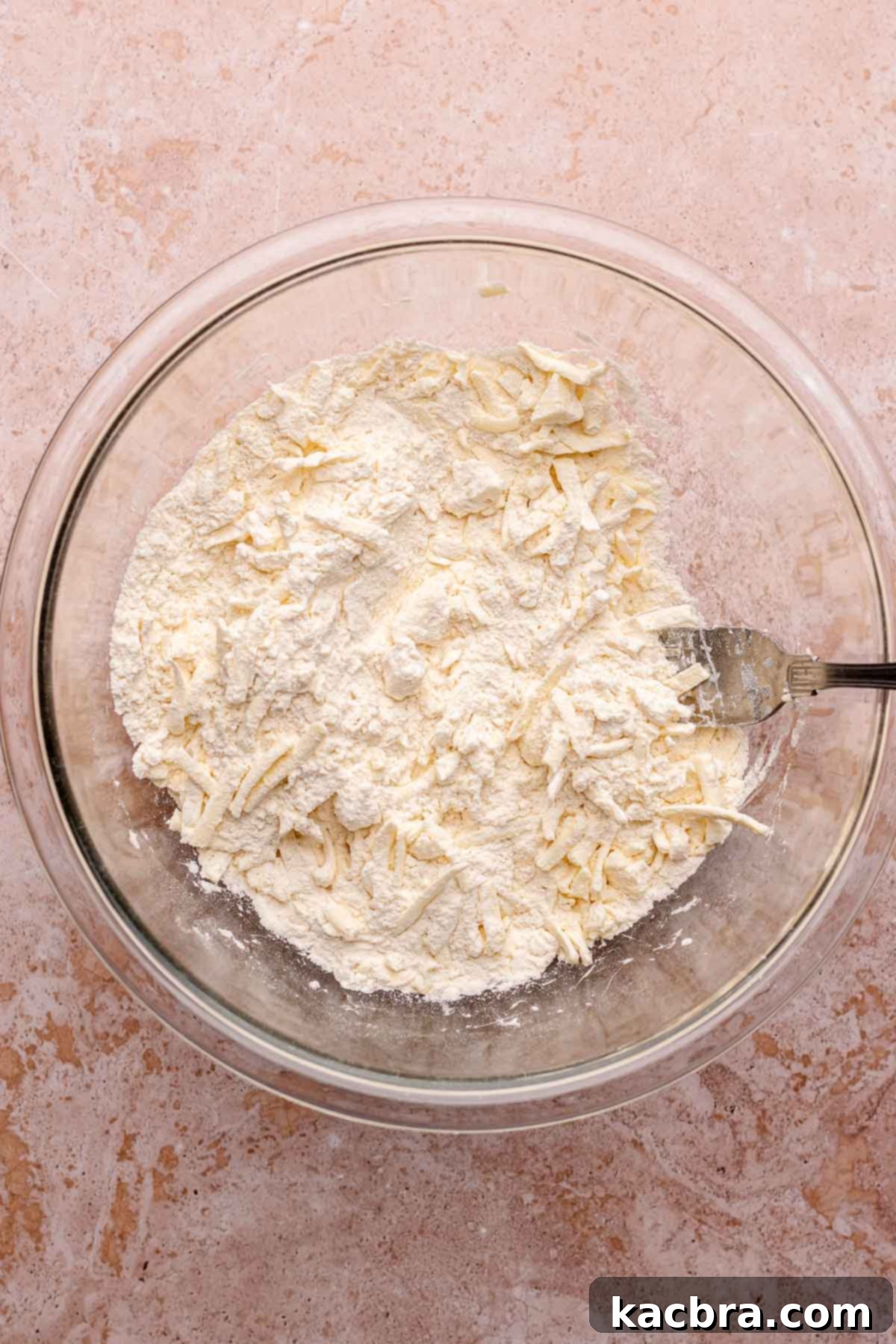A hand mixes the dry ingredients and shredded butter in a mixing bowl. This step ensures that the butter is evenly distributed throughout the flour mixture, which is crucial for creating flaky layers.
