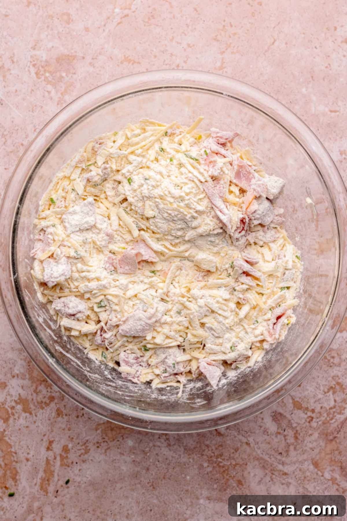 A bowl filled with all the dry ingredients for the ham and cheese scones, perfectly combined with the shredded butter. The image highlights the even distribution of ingredients and the mixture's crumbly texture.