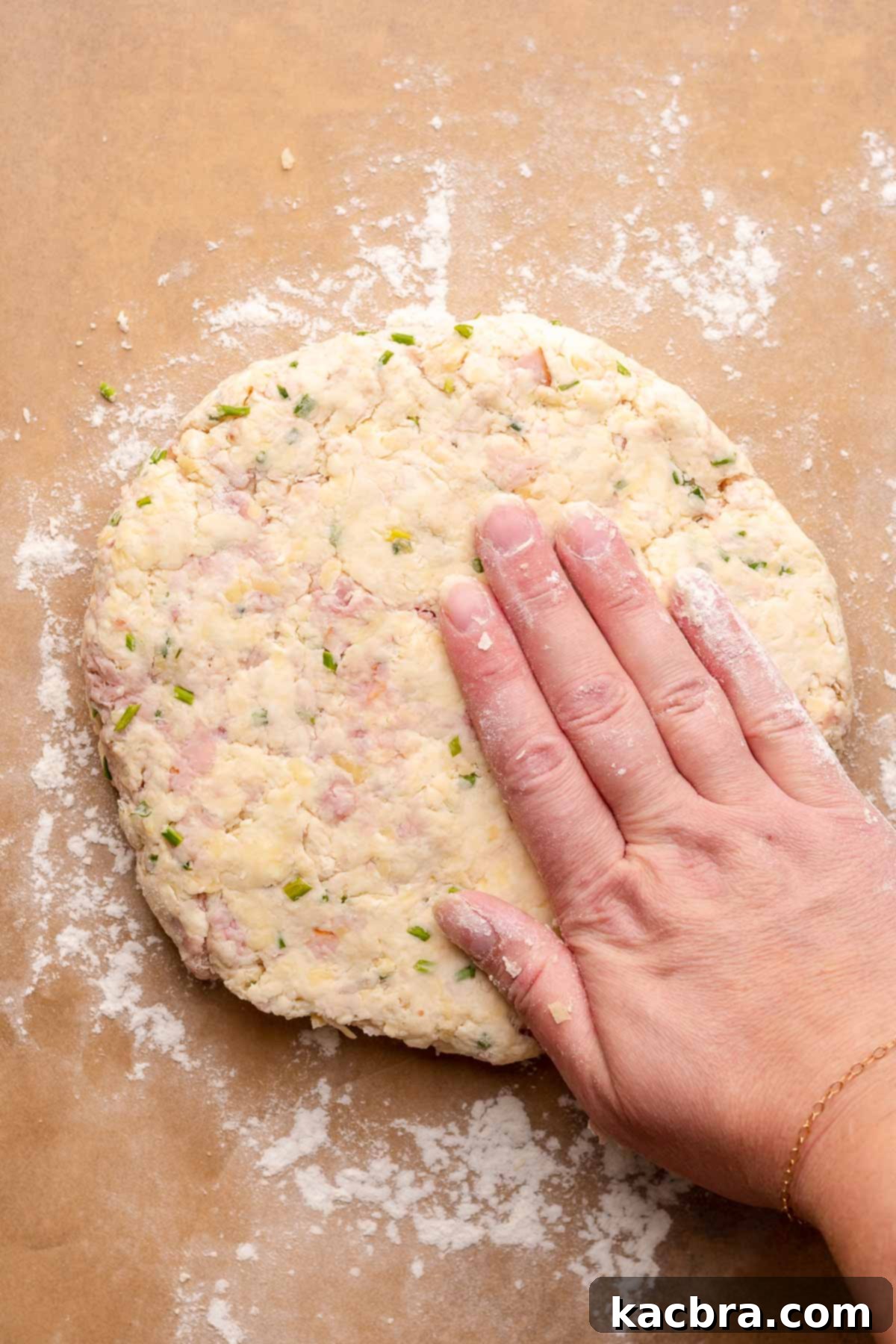 A hand gently pats the scone dough into a circle on a piece of parchment paper. The image demonstrates the proper technique for shaping the dough without overworking it.