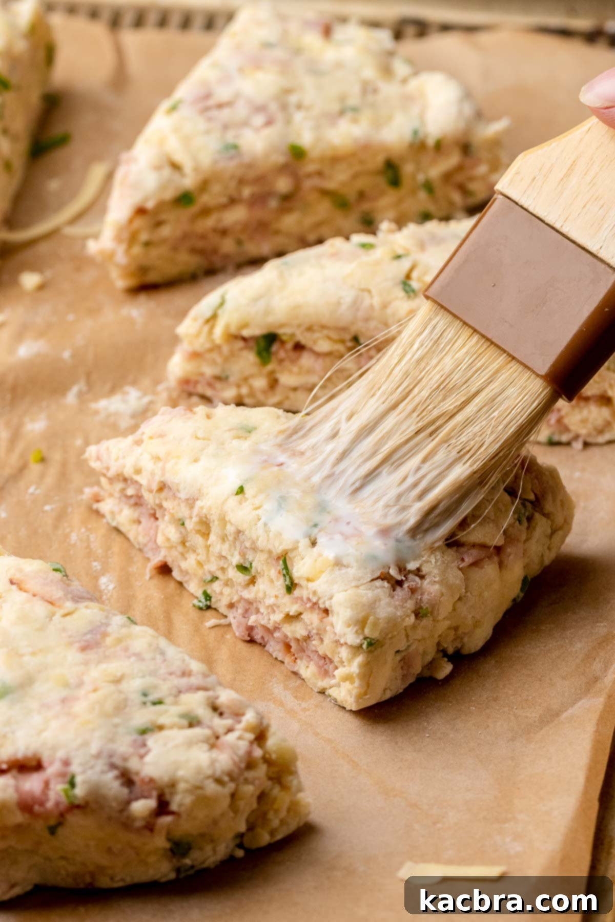 A pastry brush applying a delicate coat of milk on top of the pre-baked scones. This step helps to create a beautiful golden-brown crust.