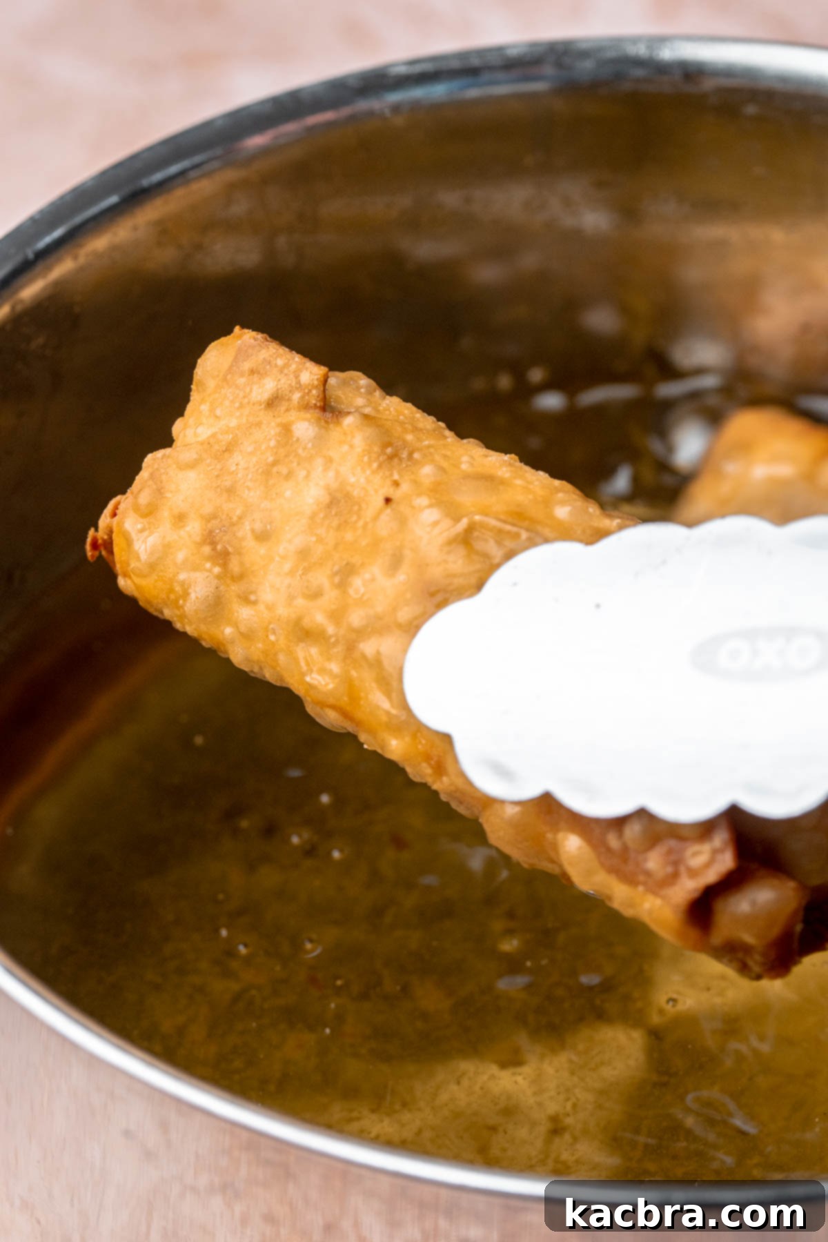 Reuben Spring Rolls 12 Tongs hold a fully fried, golden egg roll over hot oil